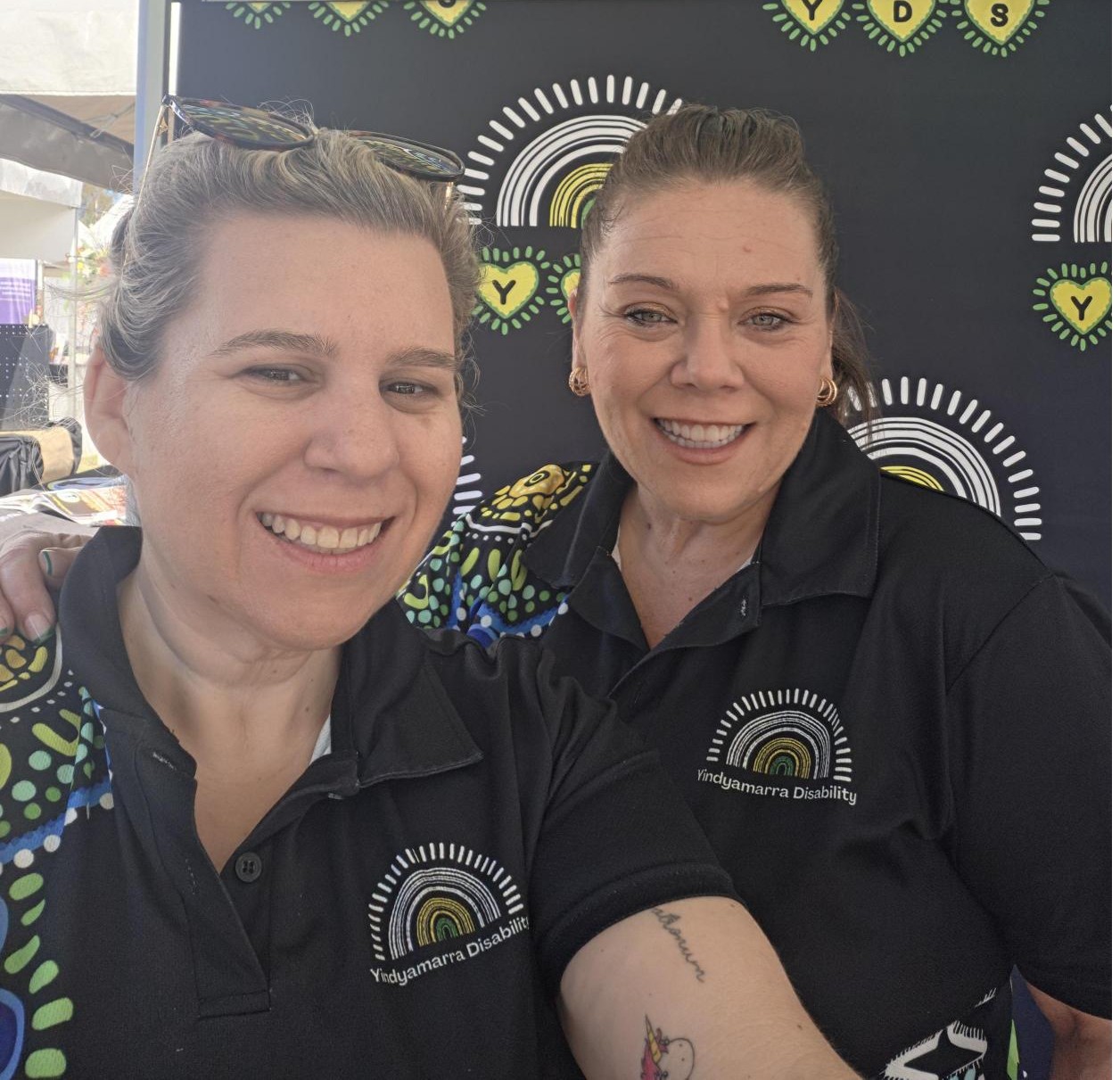 Two Yindyamarra Disability team members smiling at a community stall