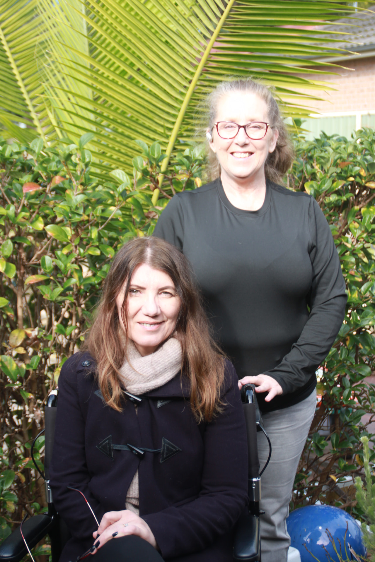 Participant using a wheelchair smiling in the garden with her support worker